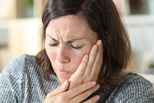 woman in pain suffering toothache touching face sitting on a couch at home
