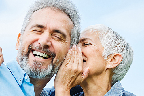 happy smiling senior couple outdoors, woman whispering into man's ear